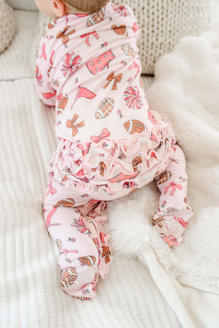 A baby lying on their stomach wearing a pink footed sleeper with a whimsical print of bows, candy canes, and candy corn, resting on a white textured blanket.