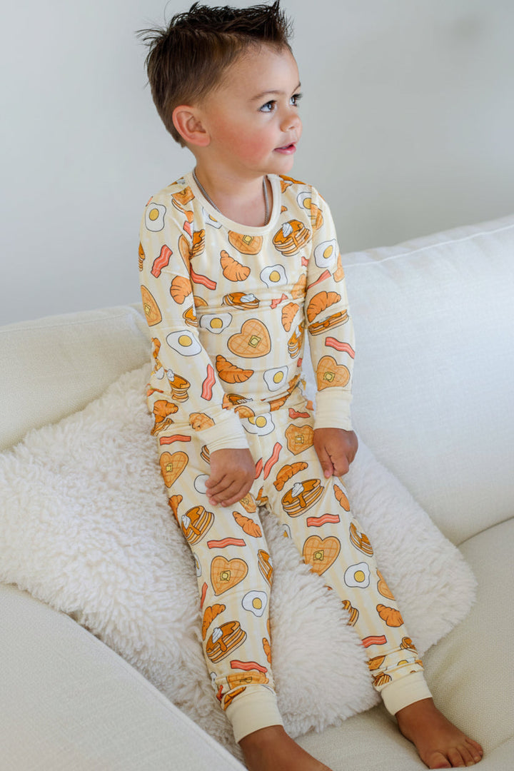 Toddler boy sitting on a couch wearing Caden Lane I Love You A Brunch long-sleeve pajama set