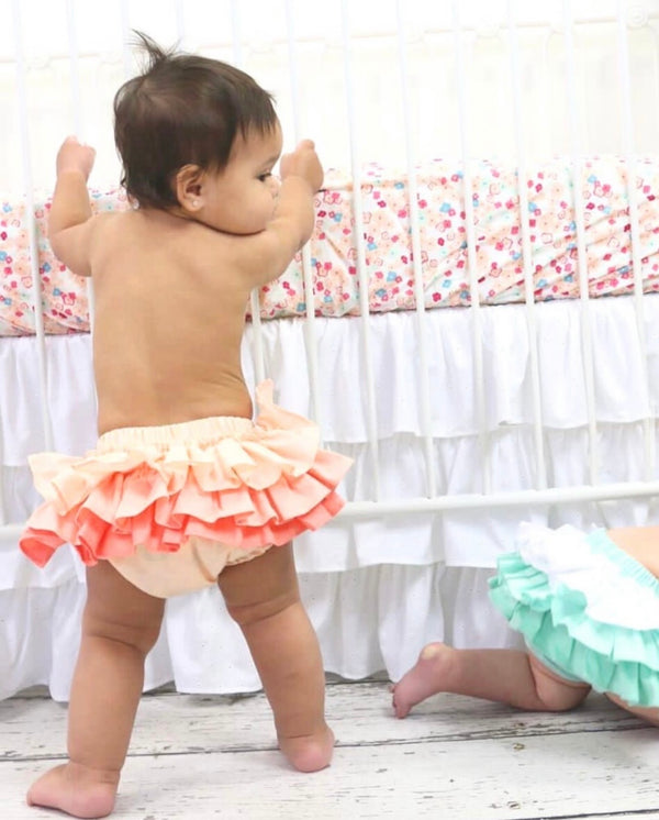 baby learning against crib wearing ruffle bloomers