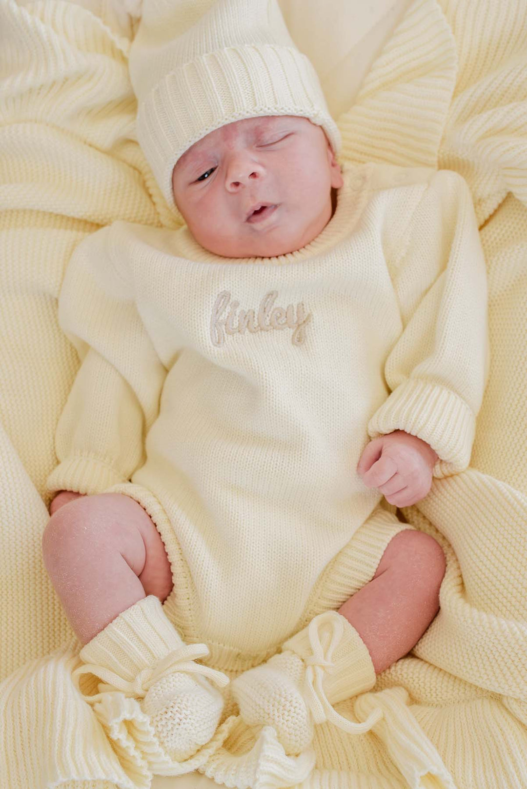 Newborn baby in Caden Lane ivory knit bubble romper, personalized "Finley" embroidery, hat, and booties
