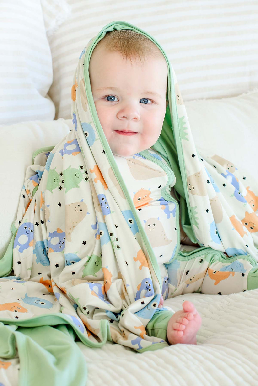 Baby wrapped in a Caden Lane sage green-trimmed Little Monsters bamboo blanket, wearing matching monster-print pajamas