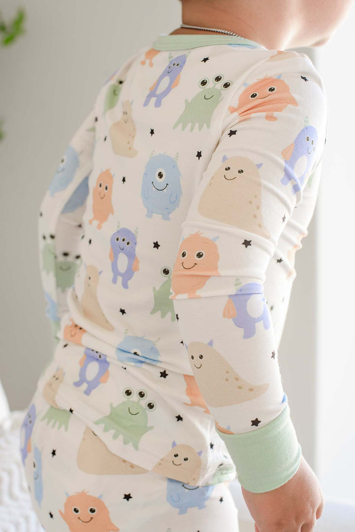 Close-up of a toddler's bak showing the monster print and sage green trim of a Caden Lane Little Monsters two-piece pajama set