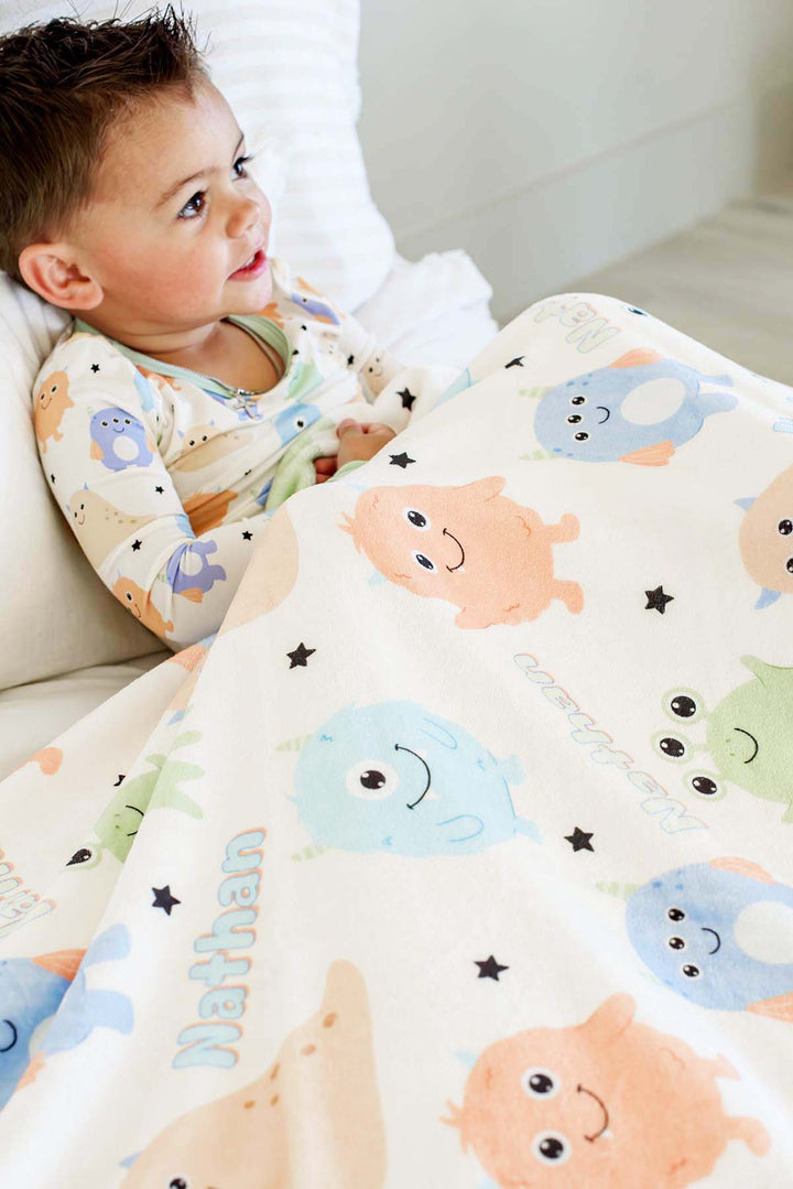 Toddler boy wrapped in a Caden Lane personalized "Nathan" Little Monsters minky blanket, wearing matching monster-print pajamas