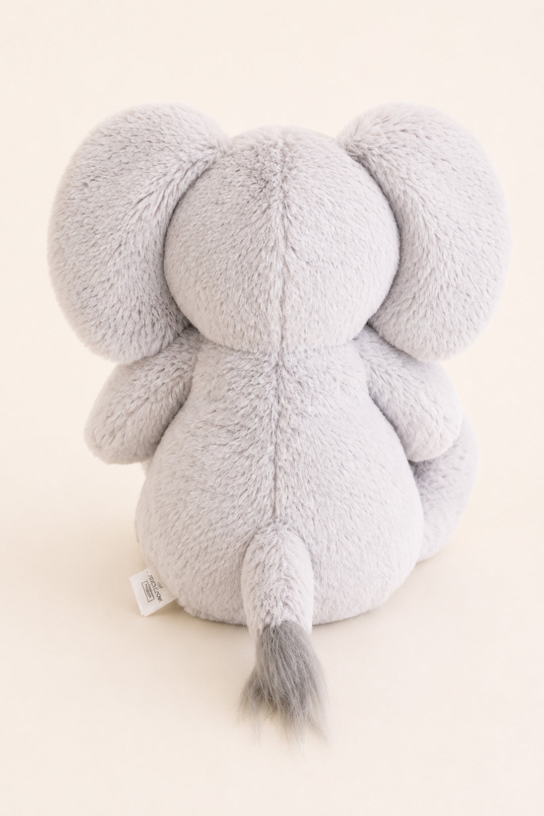 A lCaden Lane light gray plush elephant toy shown from the back, featuring soft textured fabric, large ears, and a small gray-tipped tail, photographed against a warm off-white background.