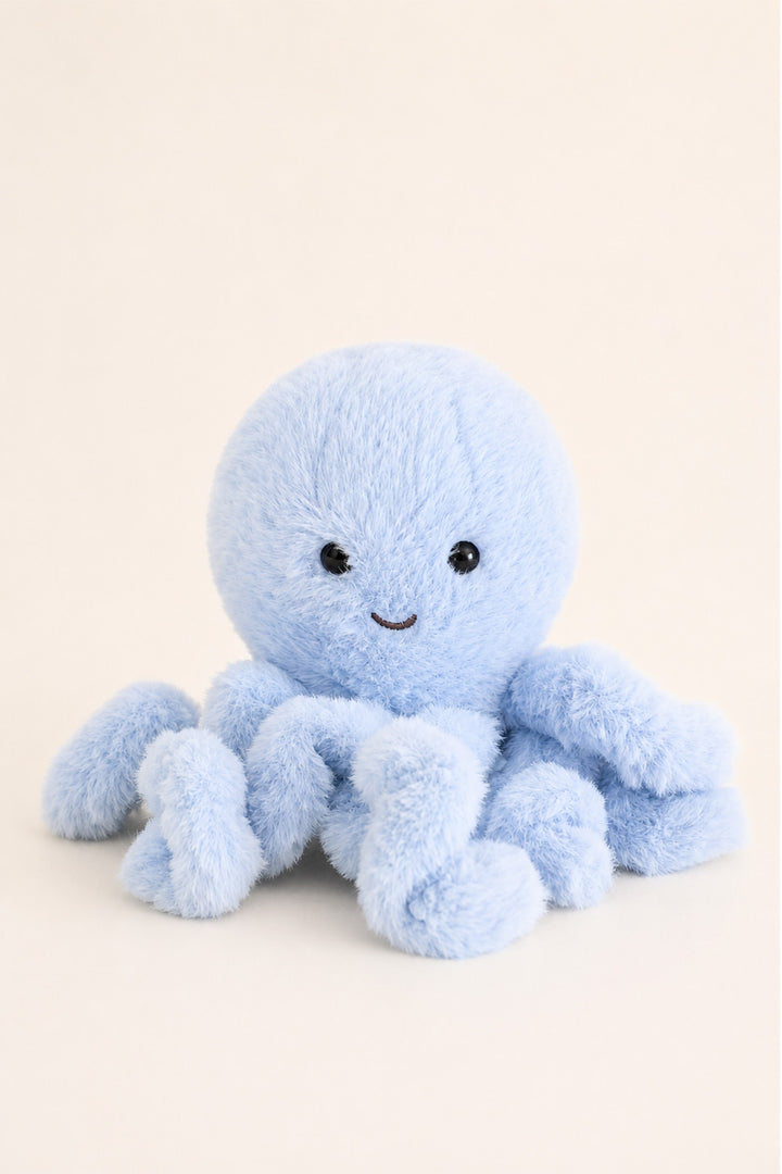 A Caden Lane light blue plush octopus toy with a soft fuzzy texture, small embroidered smile, and black bead eyes, photographed on a plain warm cream background.