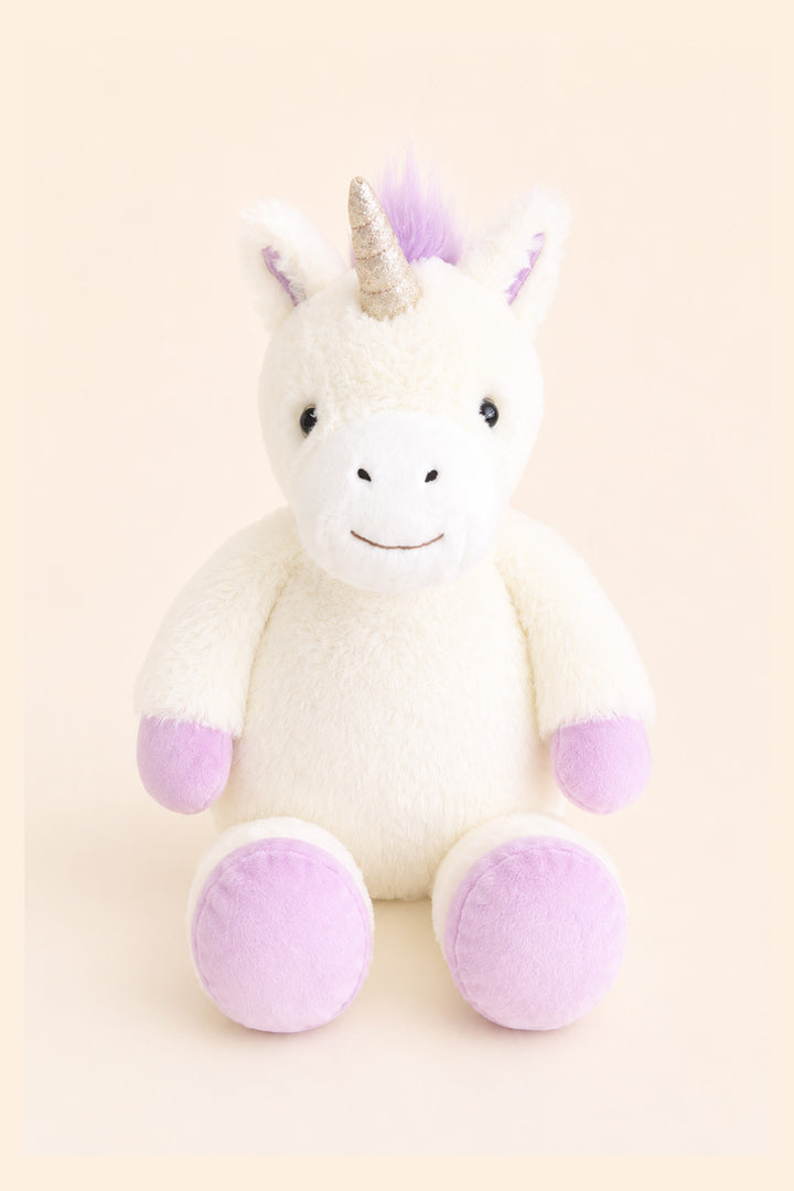 A plush Caden Lane unicorn toy with a white body, lavender-purple hooves and inner ears, a lavender mane, and a glittery gold horn, sitting against a solid pale peach background.