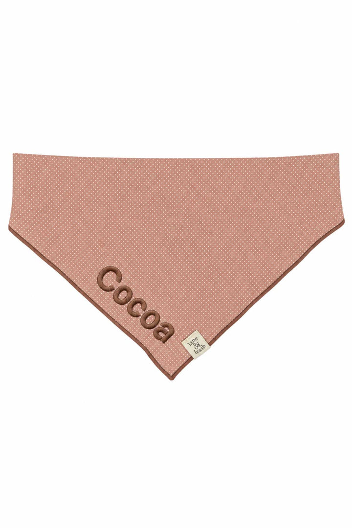 Flat lay of latte pink polka dot pet bandana with the name 'Cocoa' embroidered in brown thread