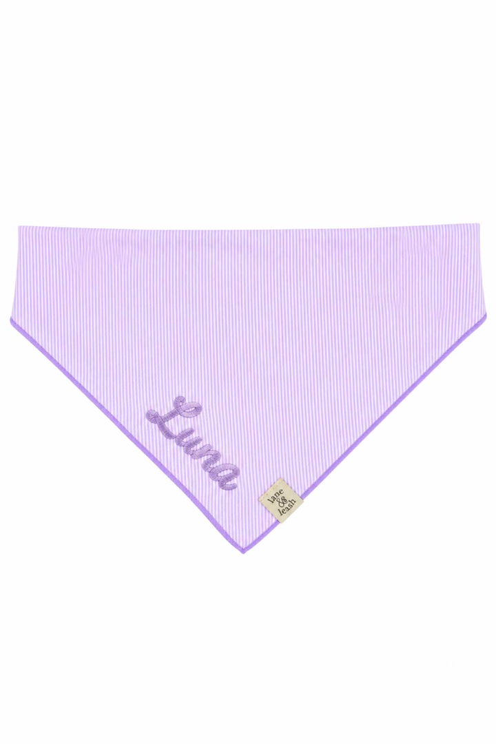 Flat lay of a solid lavender pet bandana in a triangle shape with lavender purple border and the name "Luna" embroidered in script