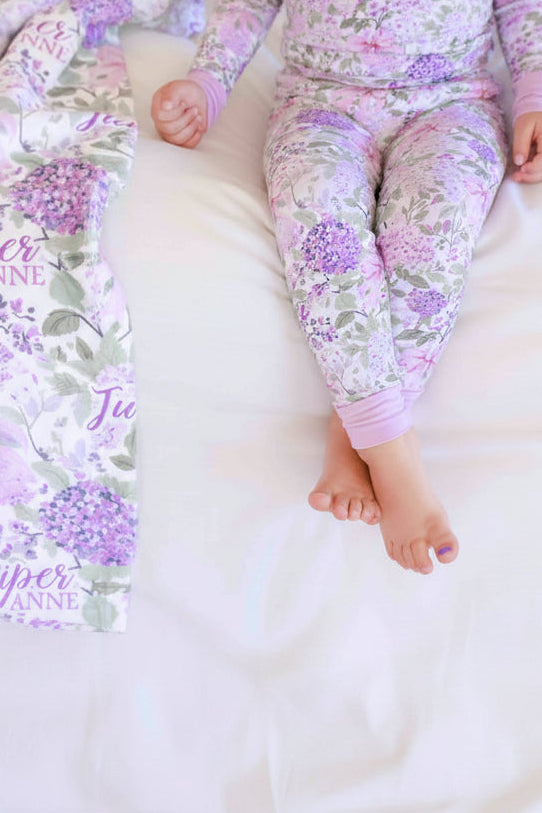 girl sitting on bed with legs crossed in lavender lullaby two piece pajama set