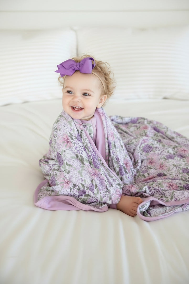 sitting baby girl looking over to the side with the lavender lullaby bamboo blanket wrapped around her shoulders 