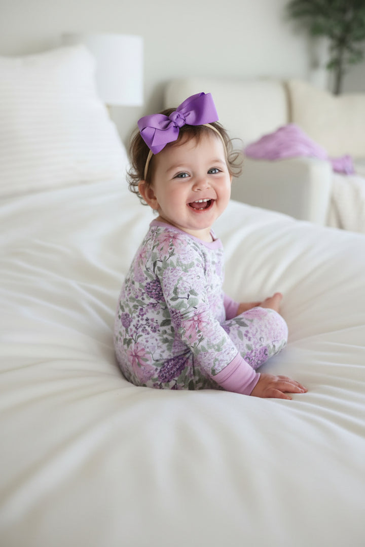 baby girl looking over her shoulder in purple hydrangea and pink bow pajama romper and amethyst ribbon bow headband