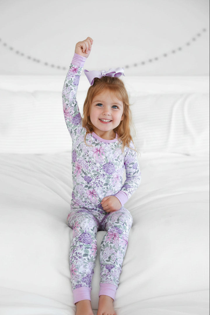 girl sitting on bed in lavender lullaby two piece pajama set