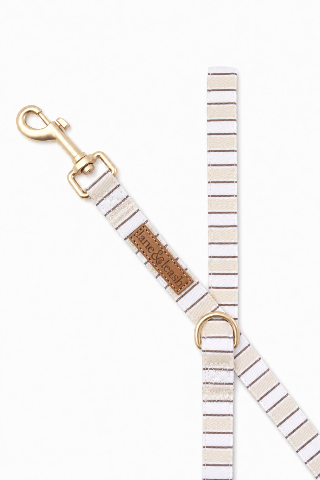 Close-up of the clasp end of the Biscuit Stripe dog leash, showing the gold-tone swivel bolt snap, a D-ring for accessories, and the leather brand tag