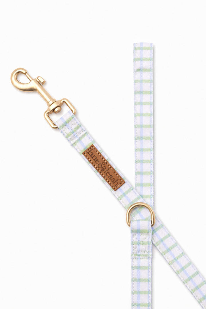 Close-up of the picnic plaid leash hardware showing the gold swivel clasp at the top, Lane & Leash leather label, and D-ring attachment point