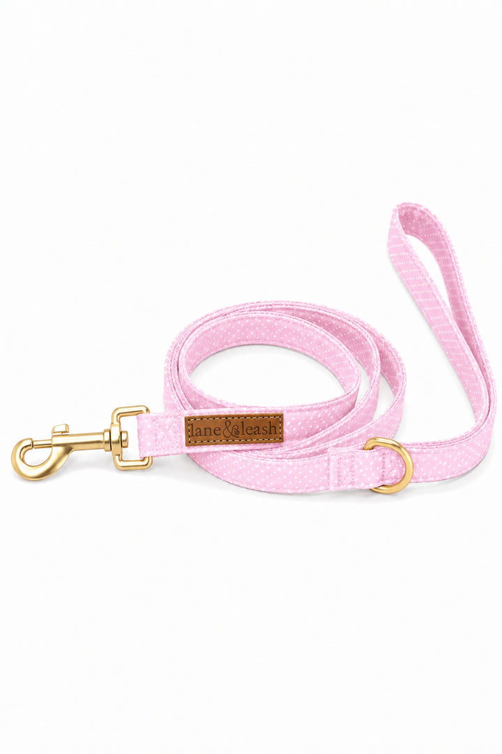 Pink polka dot heavy-duty dog leash coiled up with gold swivel clasp hook, D-ring, and leather brand label