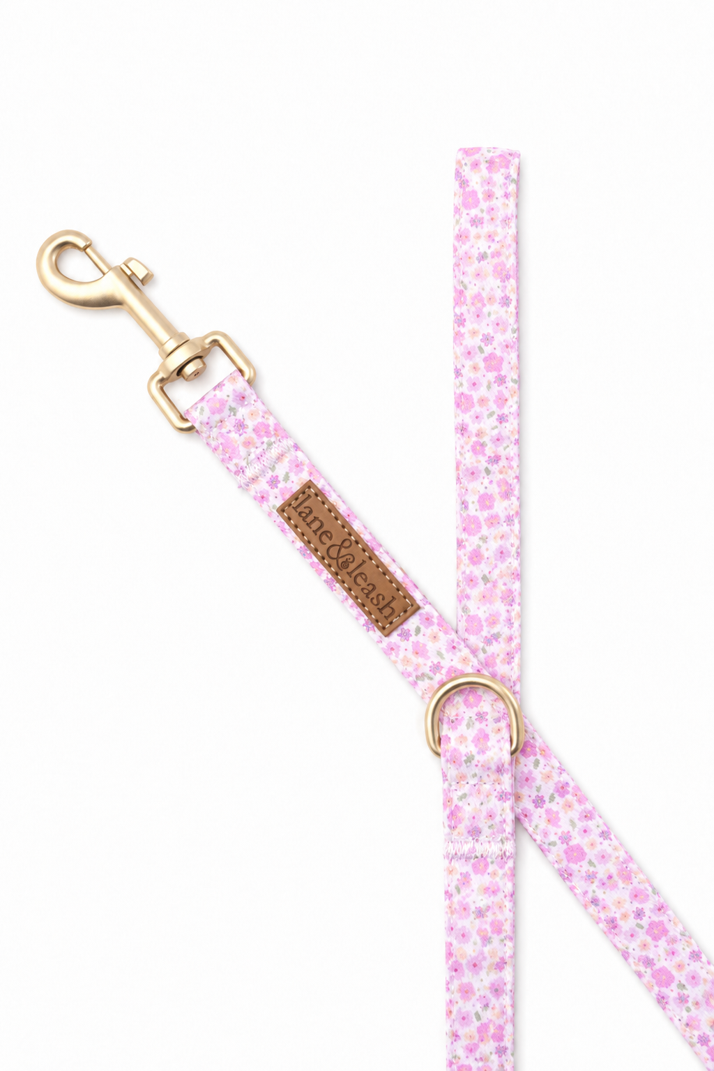 Detail shot of Scattered Blooms dog leash showing the gold snap hook hardware, adjustable slider, Lane & Leash leather tag, and D-ring attachment