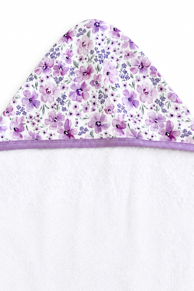Flat lay of the hood on a Caden Lane white terry kid hooded towel with lilac trim in a Lilac Dreams print featuring purple watercolor flowers and grey leaves.