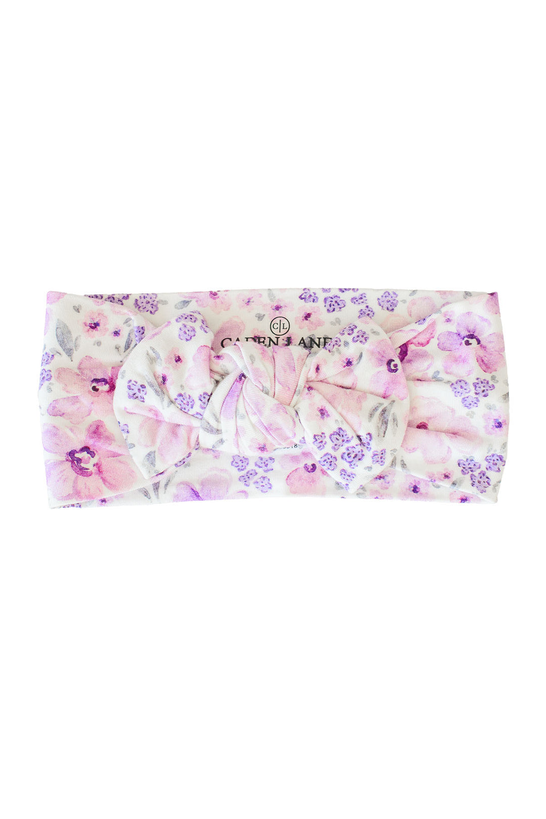 Flat lay of a Caden Lane white knit knotted bow headwrap in a Lilac Dreams print featuring pink watercolor blooms and tiny purple florals.