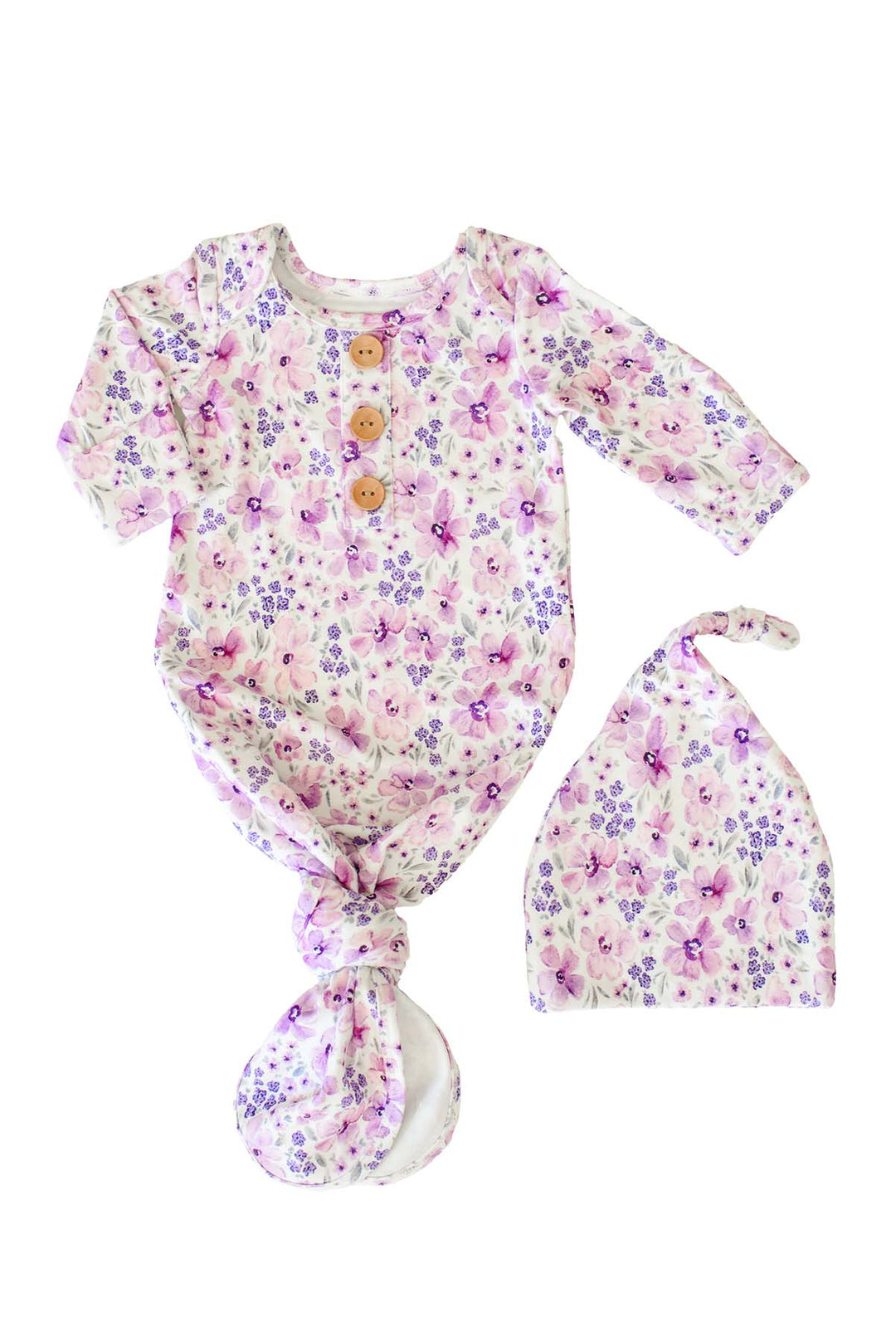 Flat lay of a Caden Lane white knit knotted gown with wooden buttons in a Lilac Dreams print featuring pink and purple flowers, paired with a matching knotted hat.