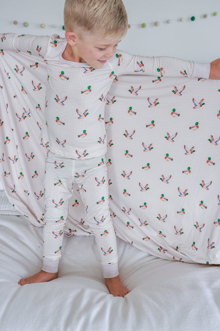 Laughing toddler lying on bed covered with little mallard duck print double-sided bamboo blanket showing the duck print fabric