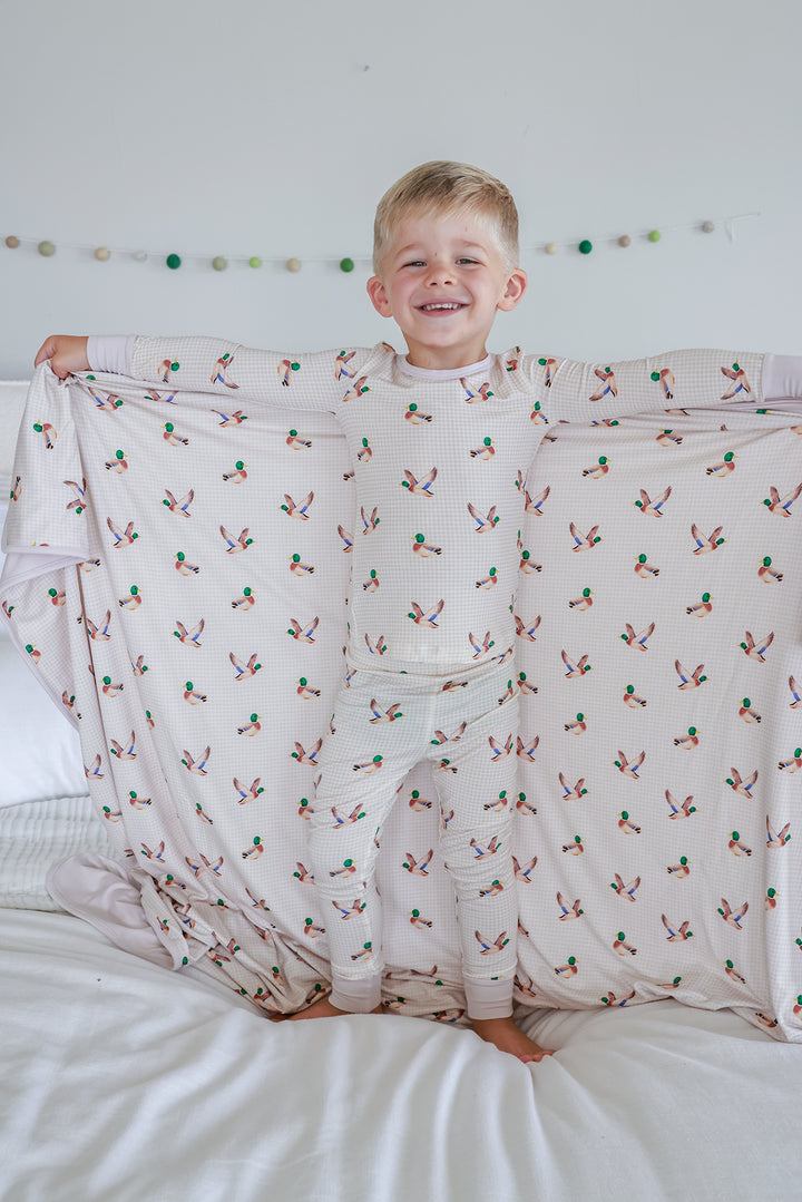 Toddler resting on bed with little mallard duck print double-sided bamboo blanket, showing mallard duck print pattern