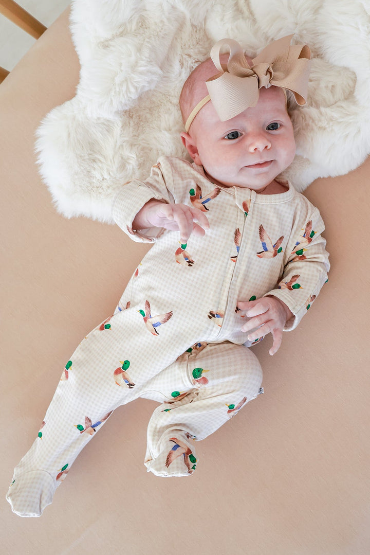 Newborn baby lying on fluffy surface wearing little mallard duck print bamboo zipper footie, alert and looking up