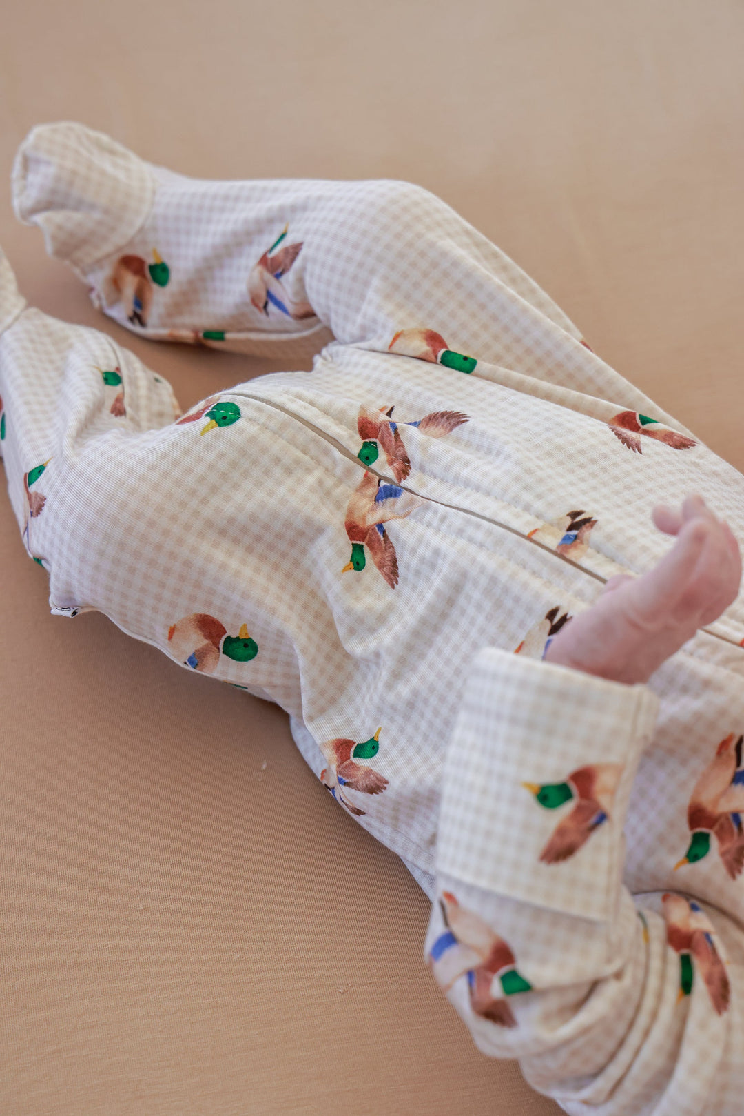 Newborn baby lying down wearing little mallard duck print bamboo zipper footie, back view showing duck print fabric and footie coverage