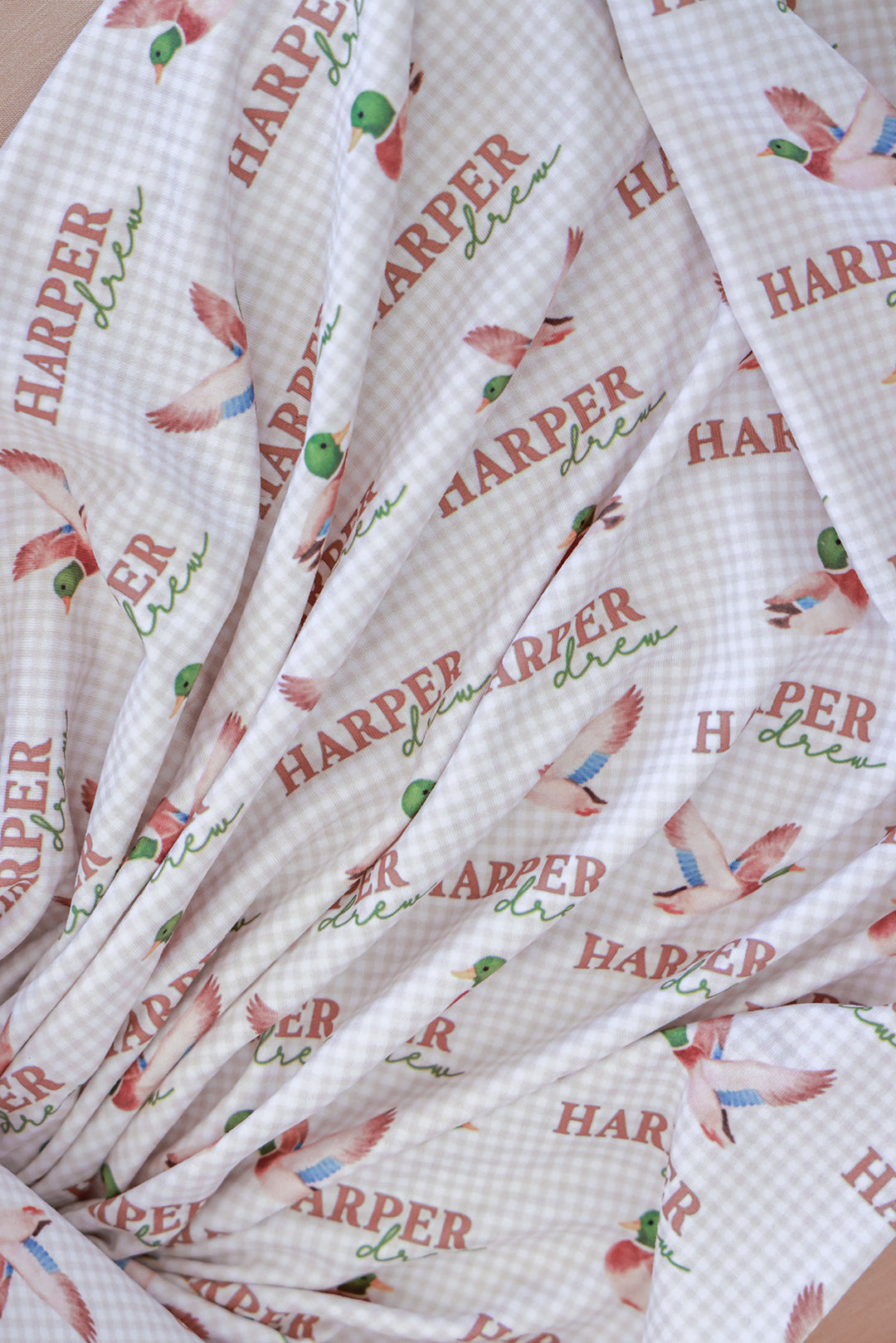 Close-up detail of personalized little mallard duck print swaddle blanket fabric showing name and flying duck pattern on gingham background