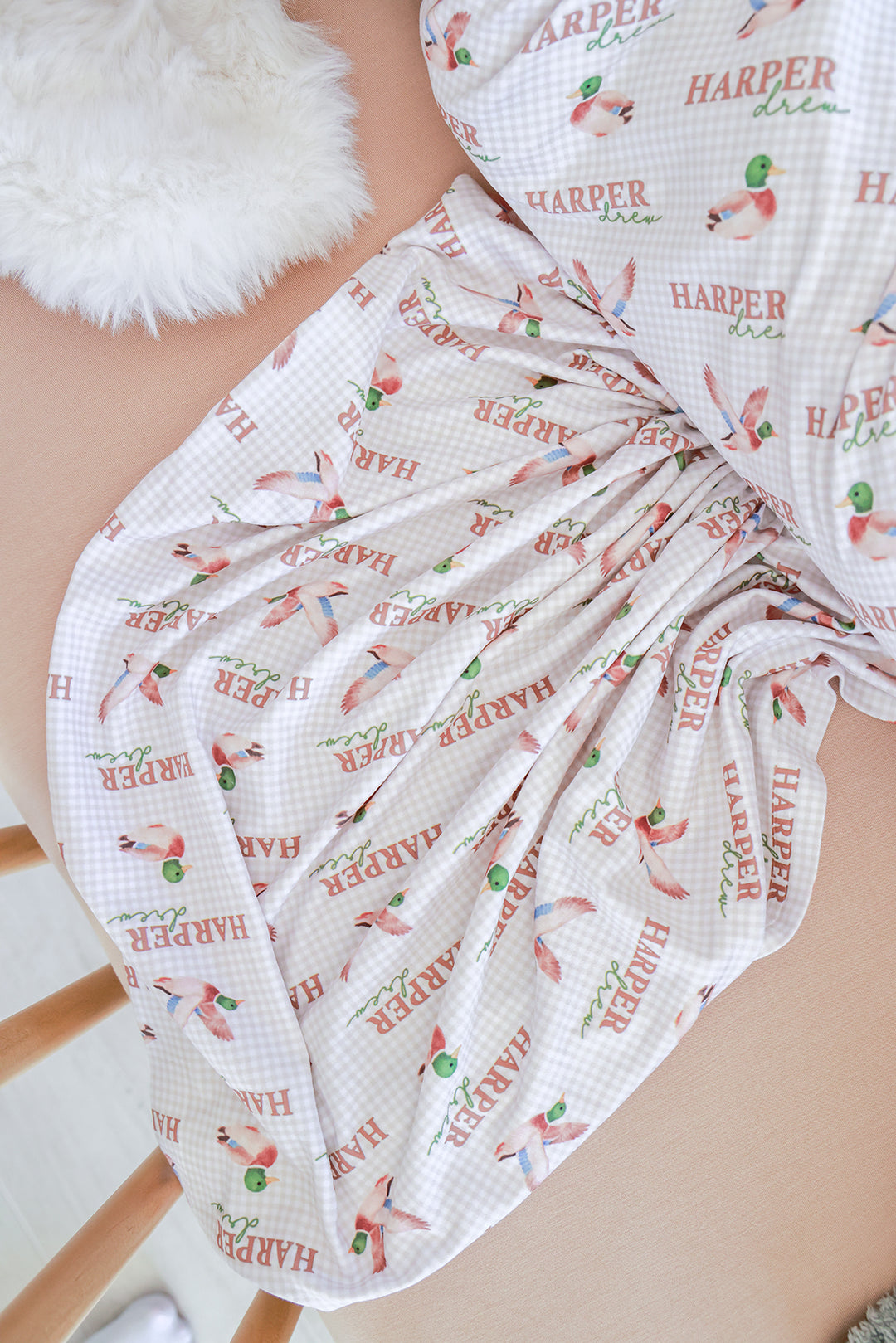 Personalized little mallard duck print swaddle blanket loosely gathered, showing name and duck pattern on gingham fabric
