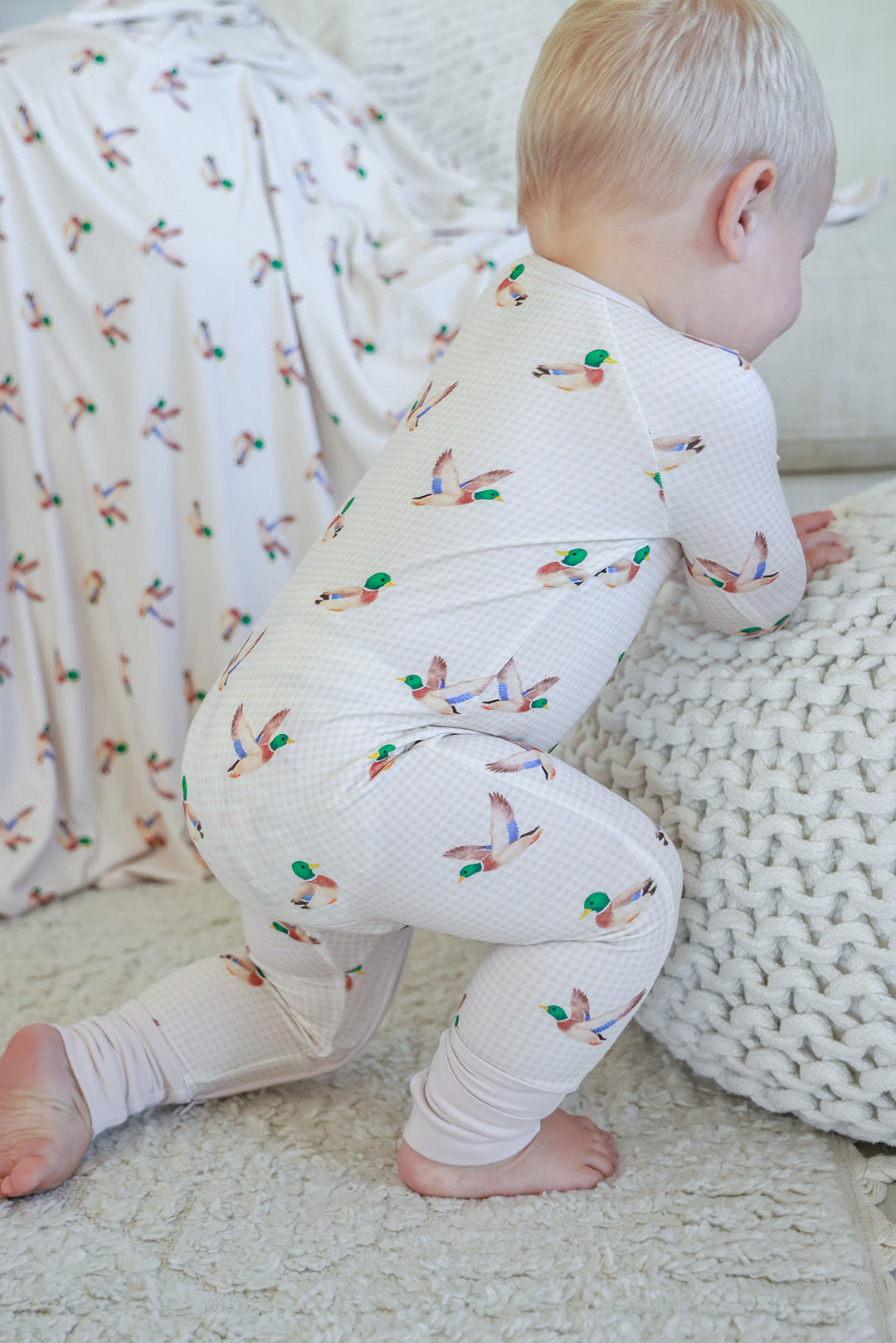 Baby crouching showing the back and side of little mallard duck print convertible zip romper with duck print pattern