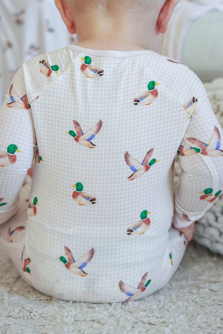 Baby sitting showing the back of little mallard duck print convertible zip romper with flying duck pattern across back