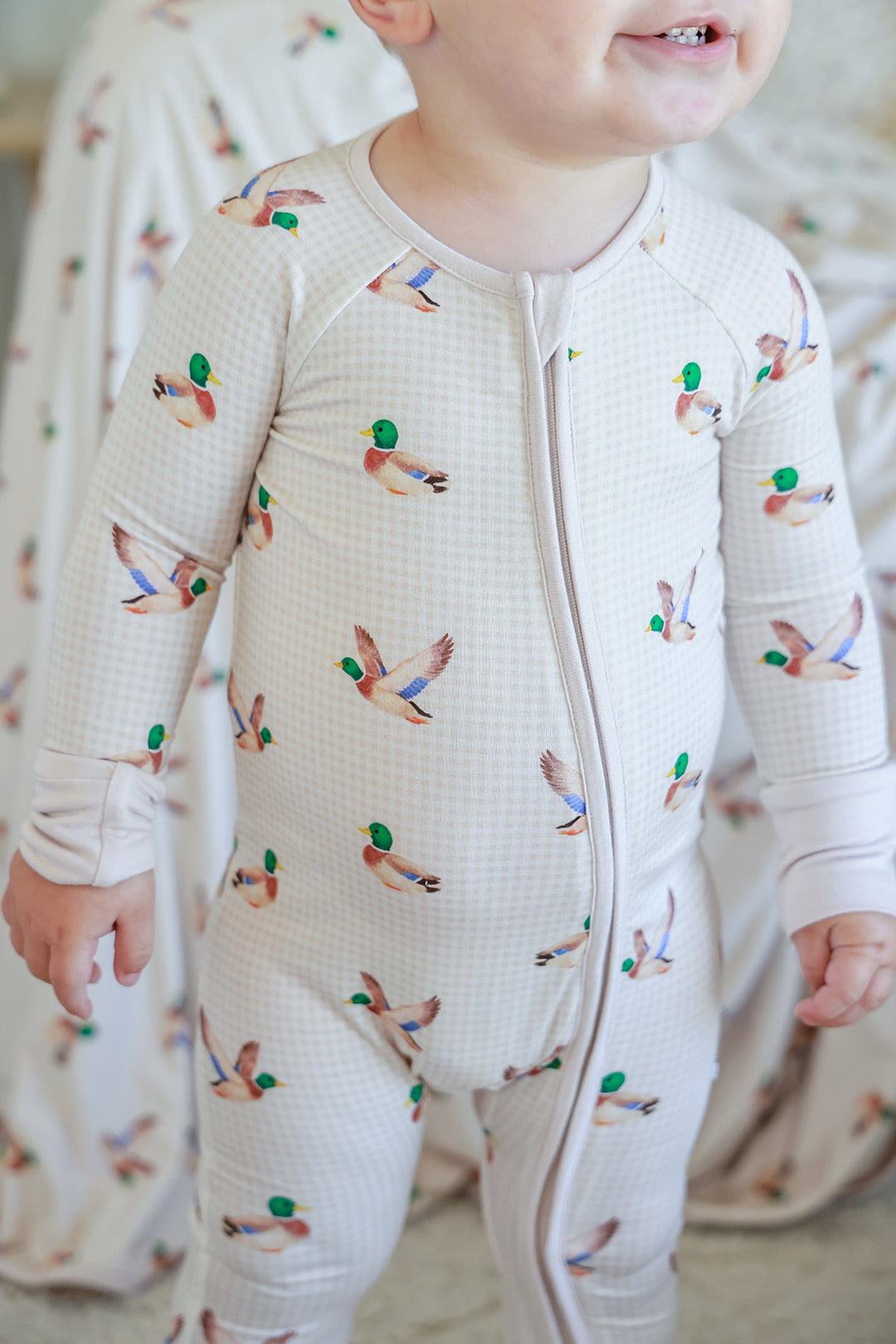 Close-up front view of toddler wearing little mallard duck print convertible zip romper showing zip and duck print detail