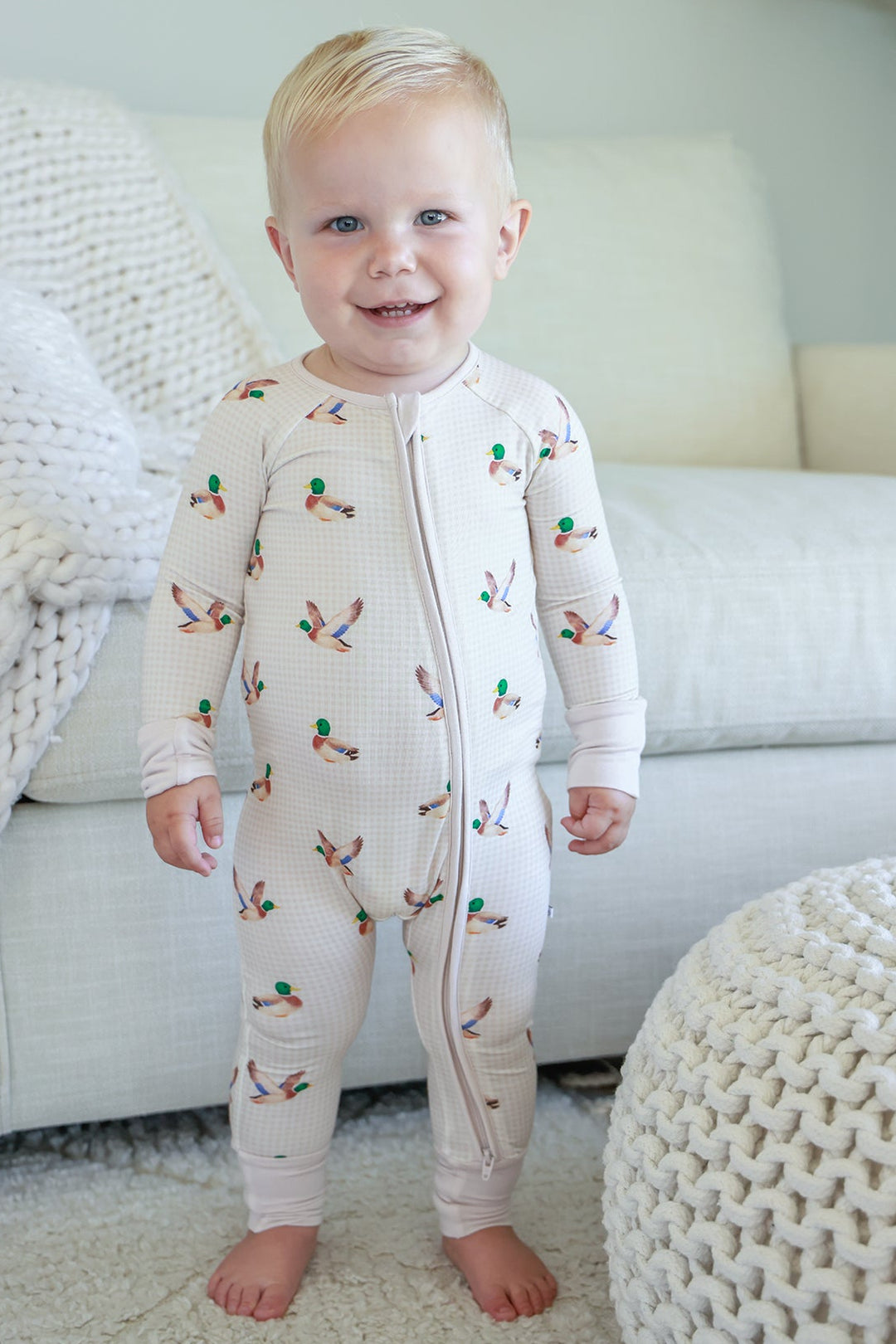 Toddler standing and smiling wearing little mallard duck print convertible zip romper, front view showing full-length zip and duck print