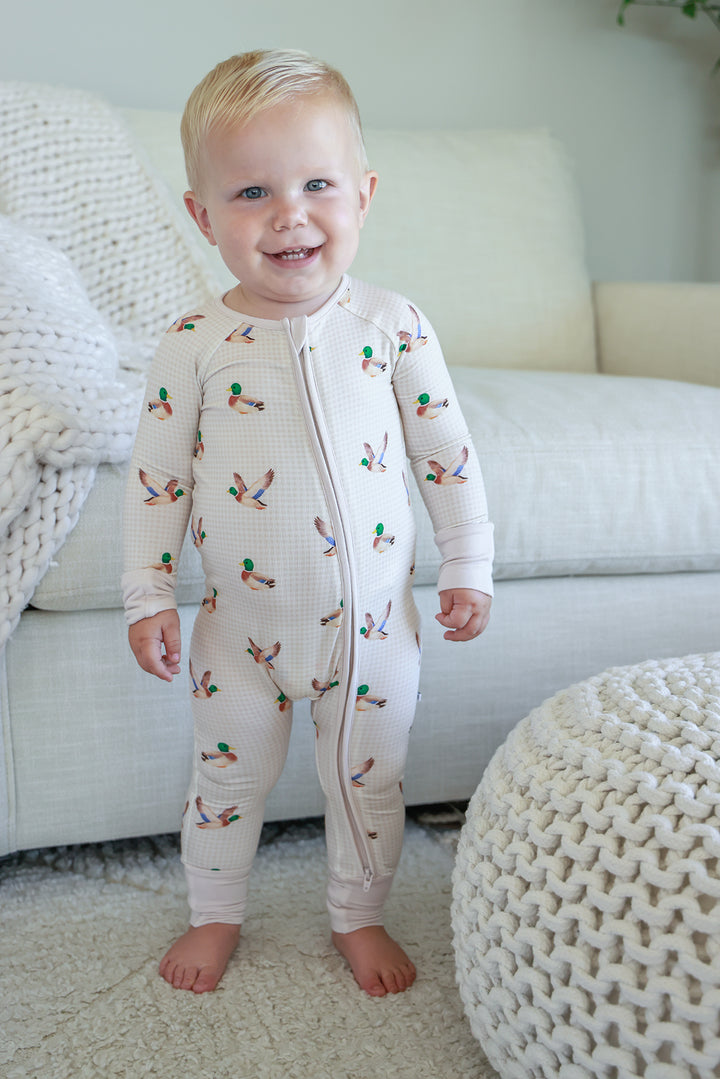 Smiling toddler standing in little mallard duck print convertible zip romper showing full front length view