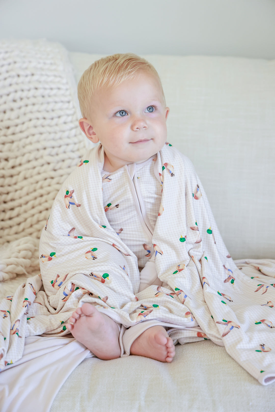 Toddler sitting and smiling wrapped in little mallard duck print double-sided bamboo blanket