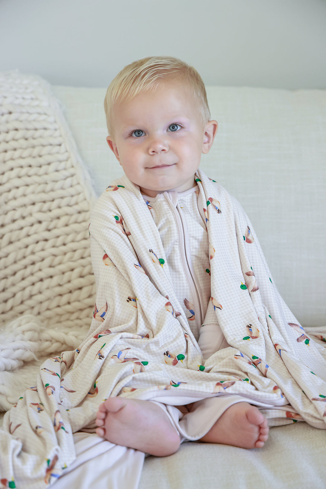 Smiling toddler lying on bed wrapped in little mallard duck print double-sided bamboo blanket, overhead view