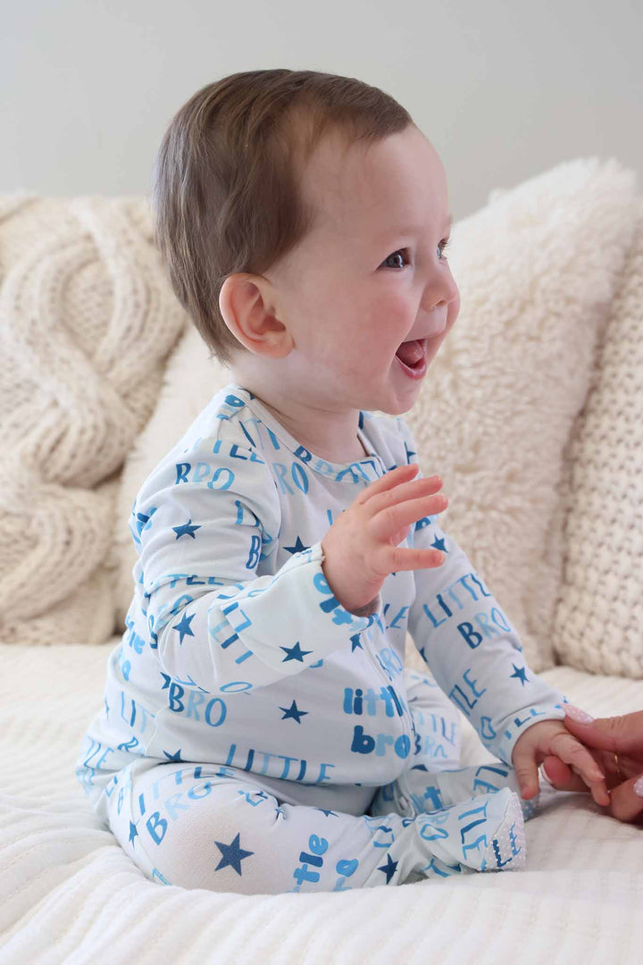 smiling baby boy sitting wearing the little bro star zipper footie 