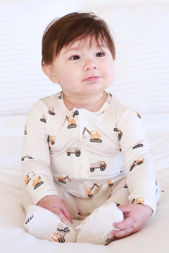 sitting baby boy in little builder cream zipper footie pajama 
