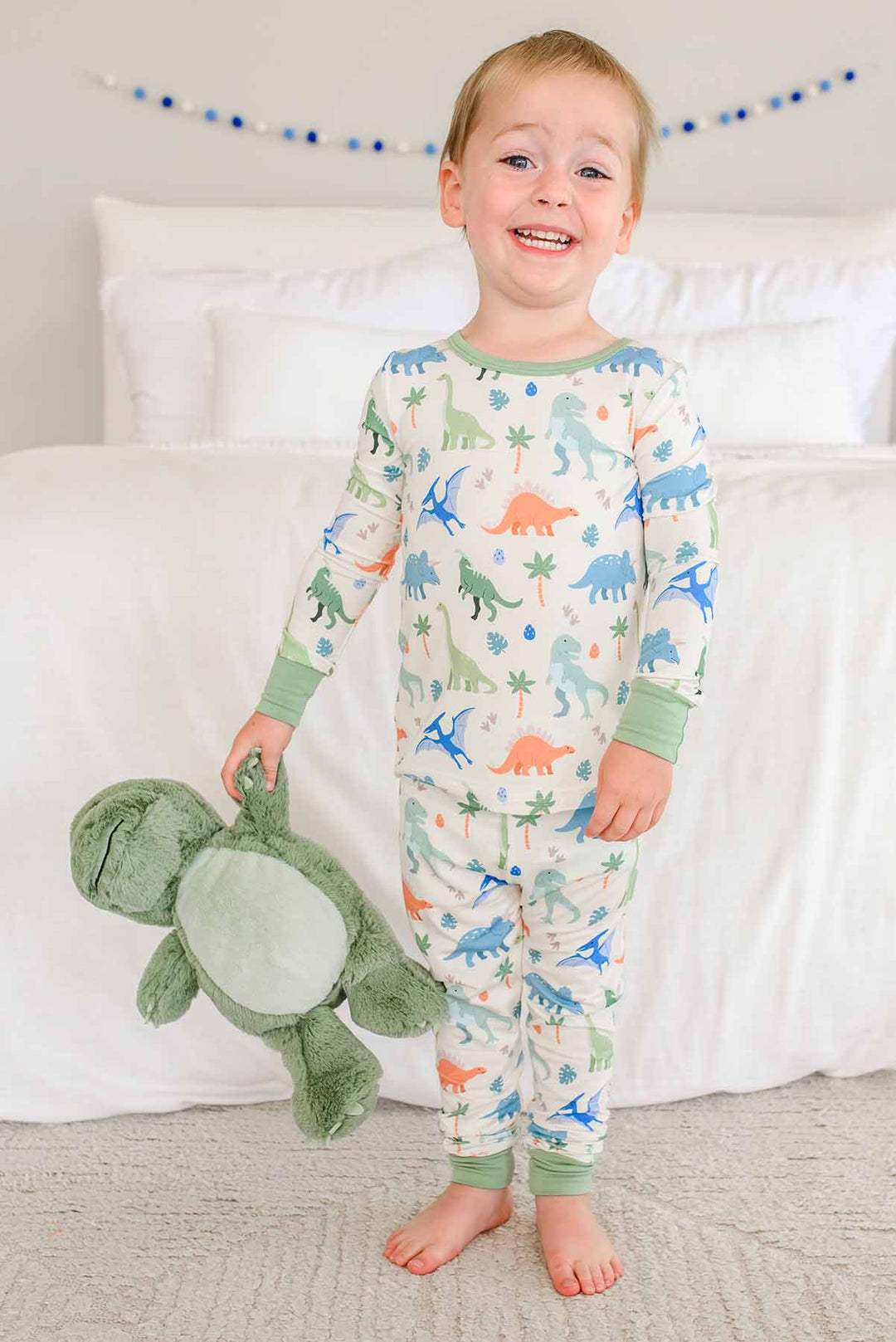 kid wearing colorful dinosaur pajamas holding a stuffed t-rex