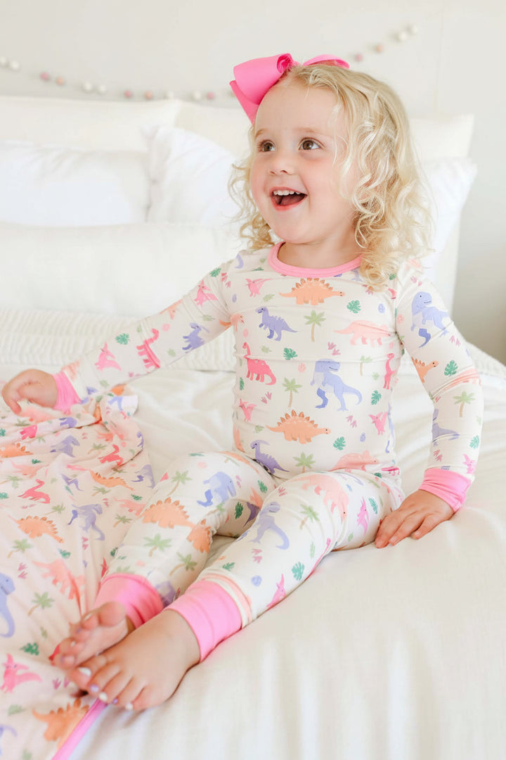 girl sitting on bed in little fossil pink two piece pajama set with a pink ribbon clip bow