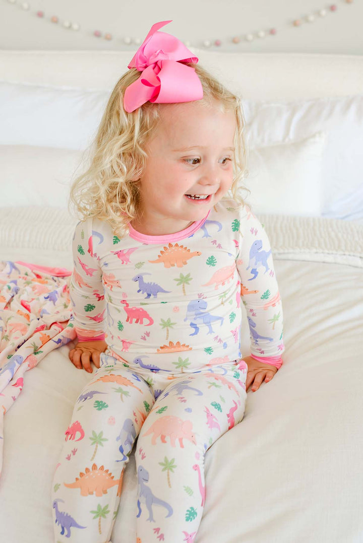 girl sitting on bed in little fossil pink long sleeve and pant two piece pajama set 