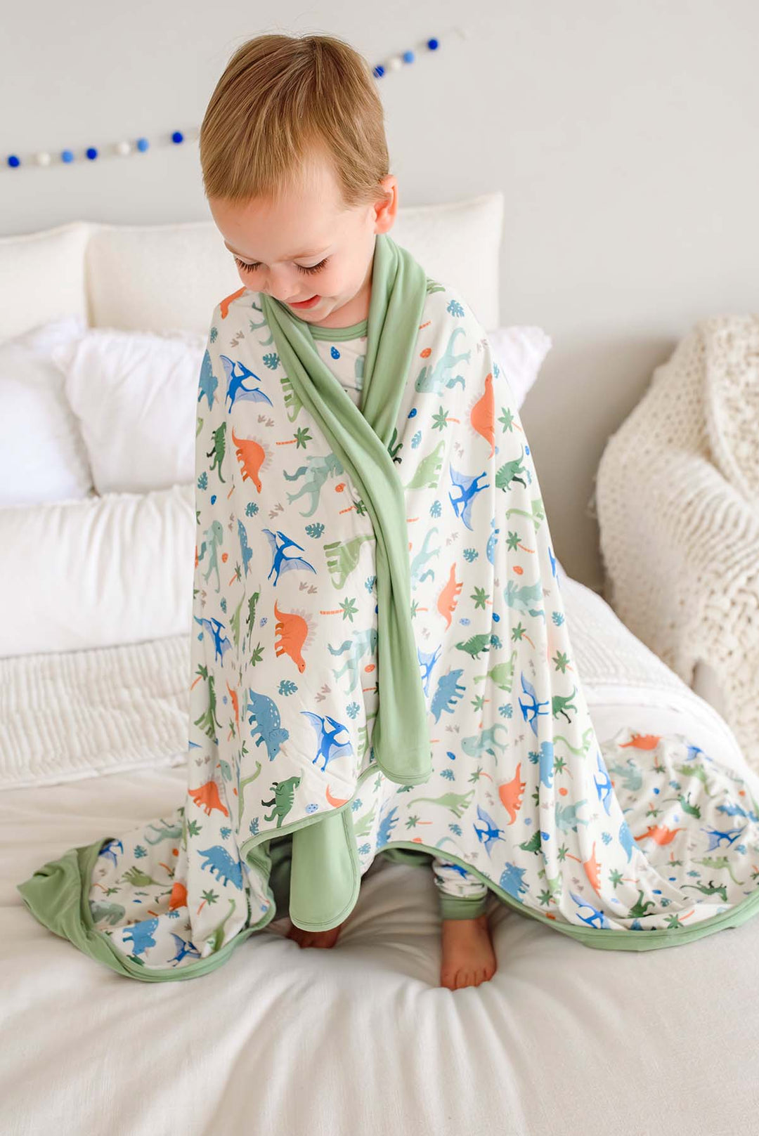 boy standing on bed with little fossil bamboo blanket wrapped around him