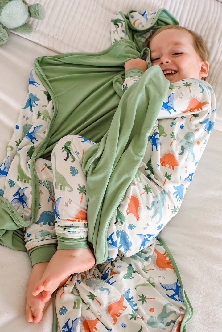 boy laying on bed holding the little fossil neutral blanket with matching pajama set