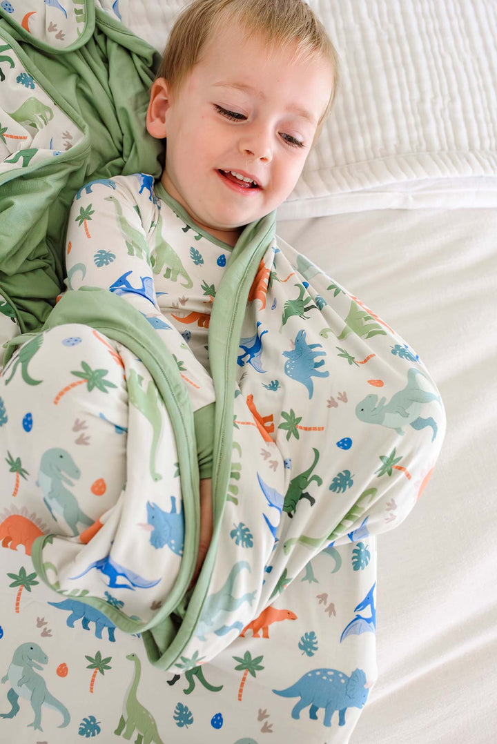 boy wrapped in little fossil bamboo blanket wearing the matching pajama set