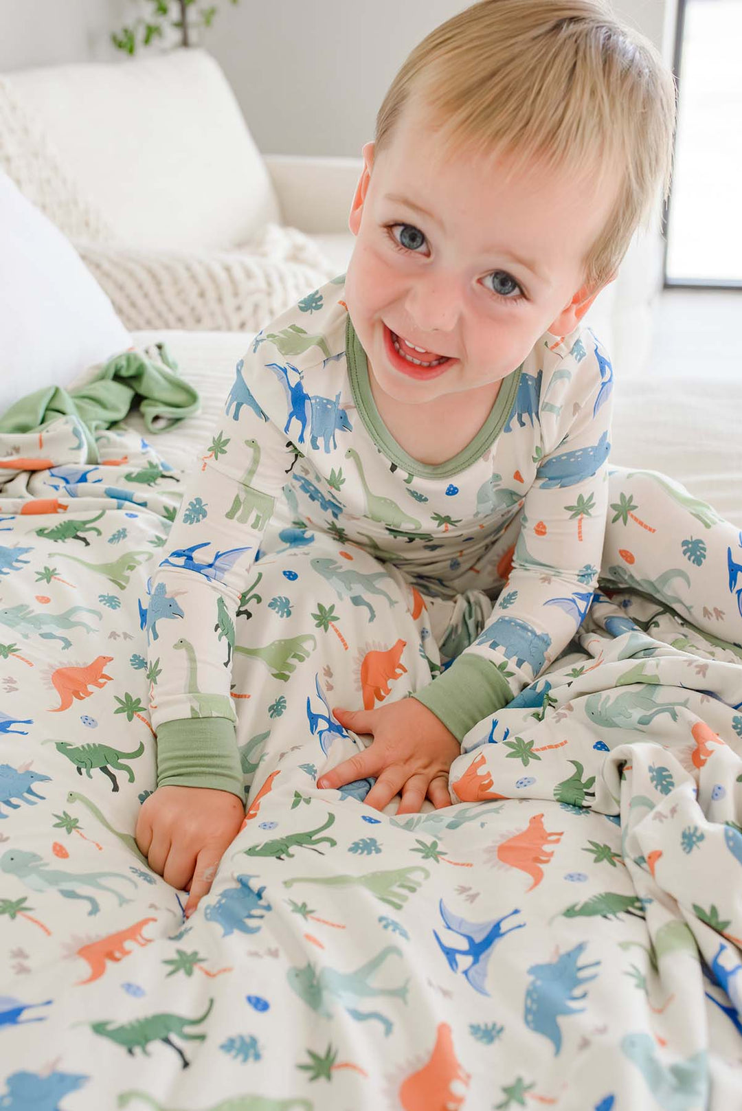 boy wearing the neutral dinosaur long sleeve pajama set pointing to the matching bamboo blanket