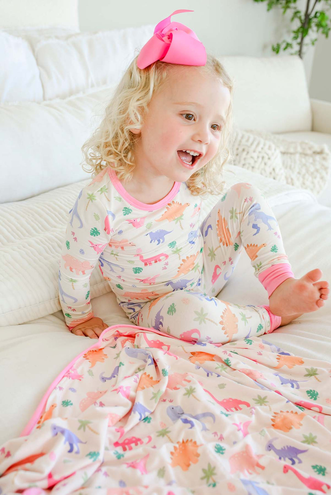 happy girl with pastel dinosaur double sided bamboo blanket and 2pc pajama set