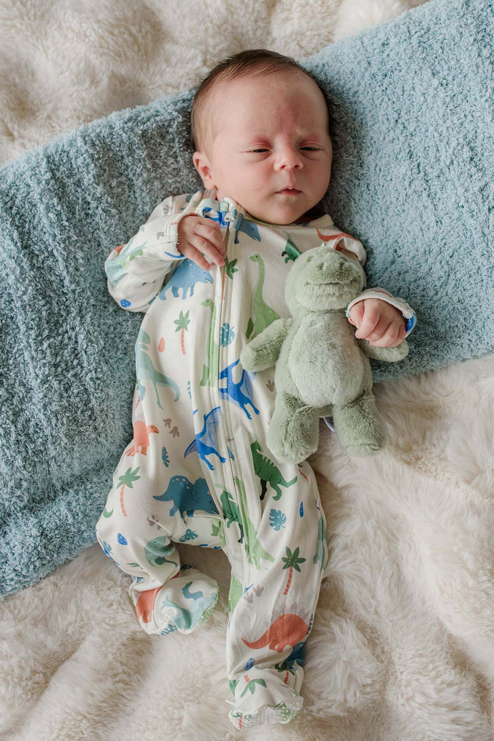baby boy laying down wearing a dinosaur footie holding a small stuffed t-rex
