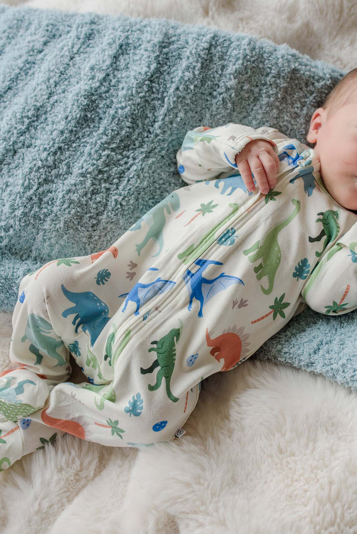 baby laying on blue blanket in neutral dinosaur footie 