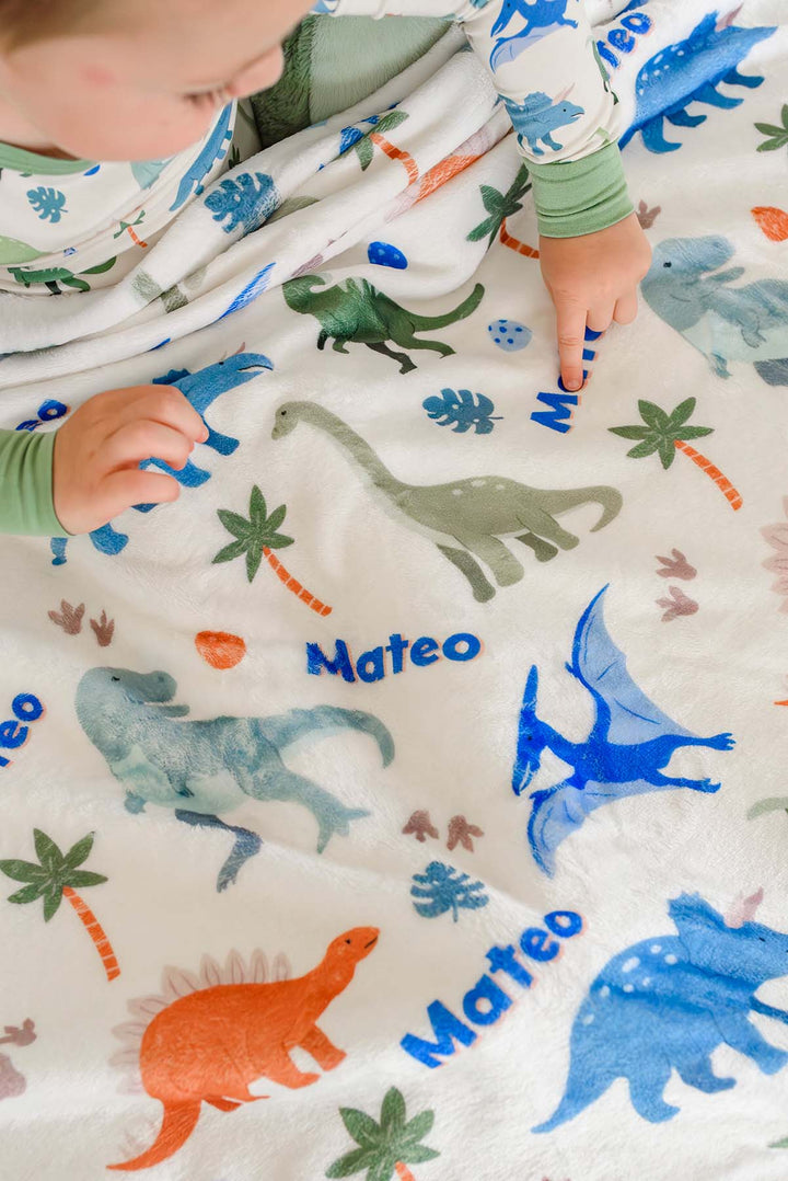 boy pointing to name on little fossil personalized blanket with dinosaurs