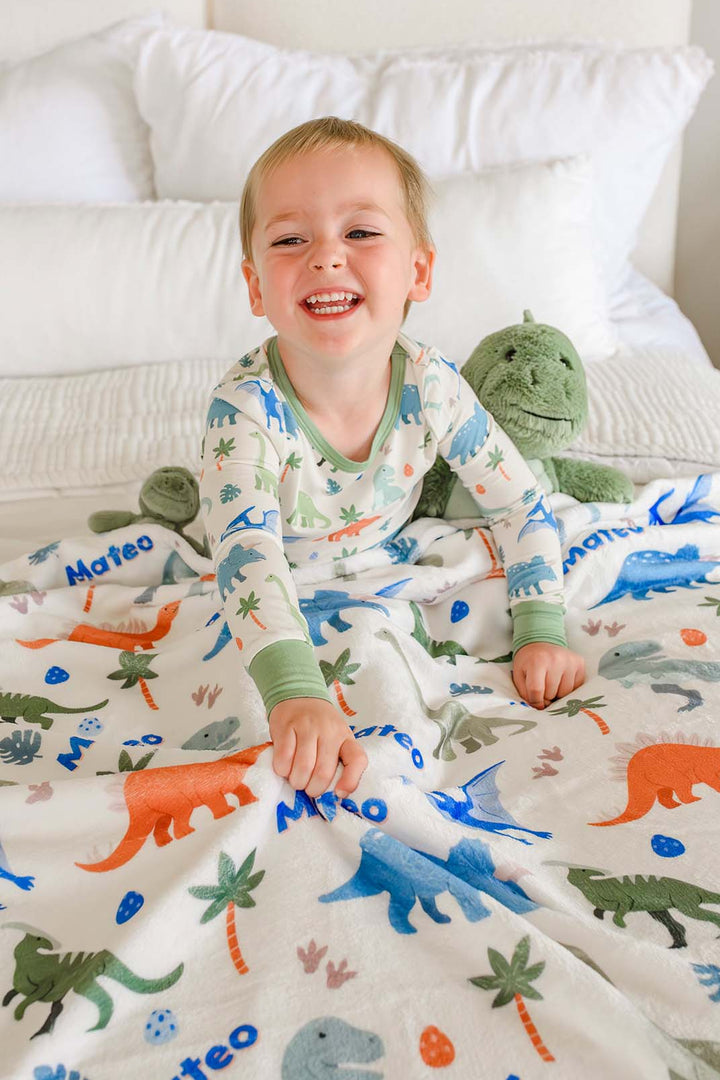 kid sitting on bed in little fossil neutral two piece pajama set with personalized blanket on lap